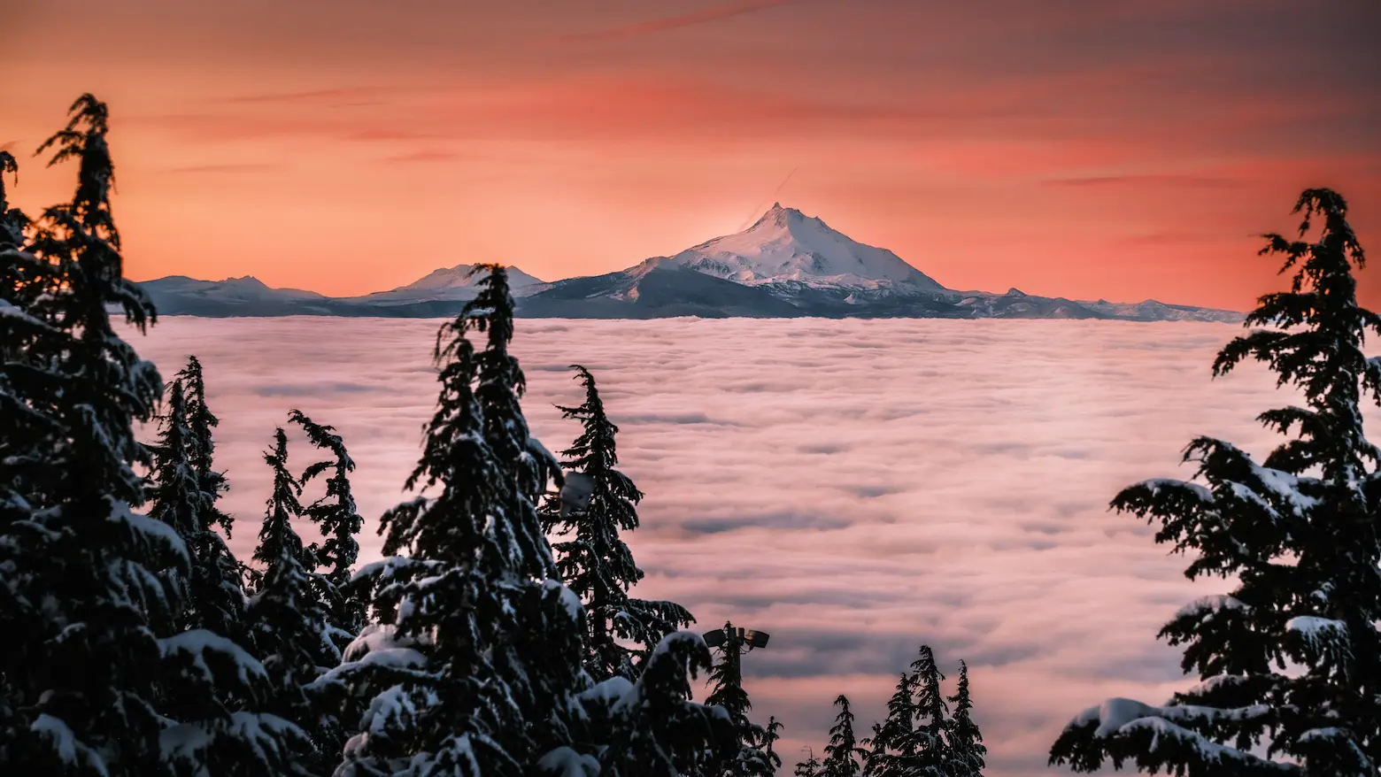 sunrise with a mountain in the background with clouds below the viewer