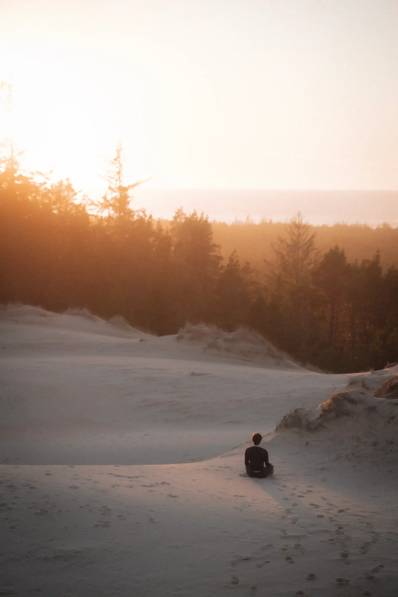 person sitting cross-legged near sand dune at sunset