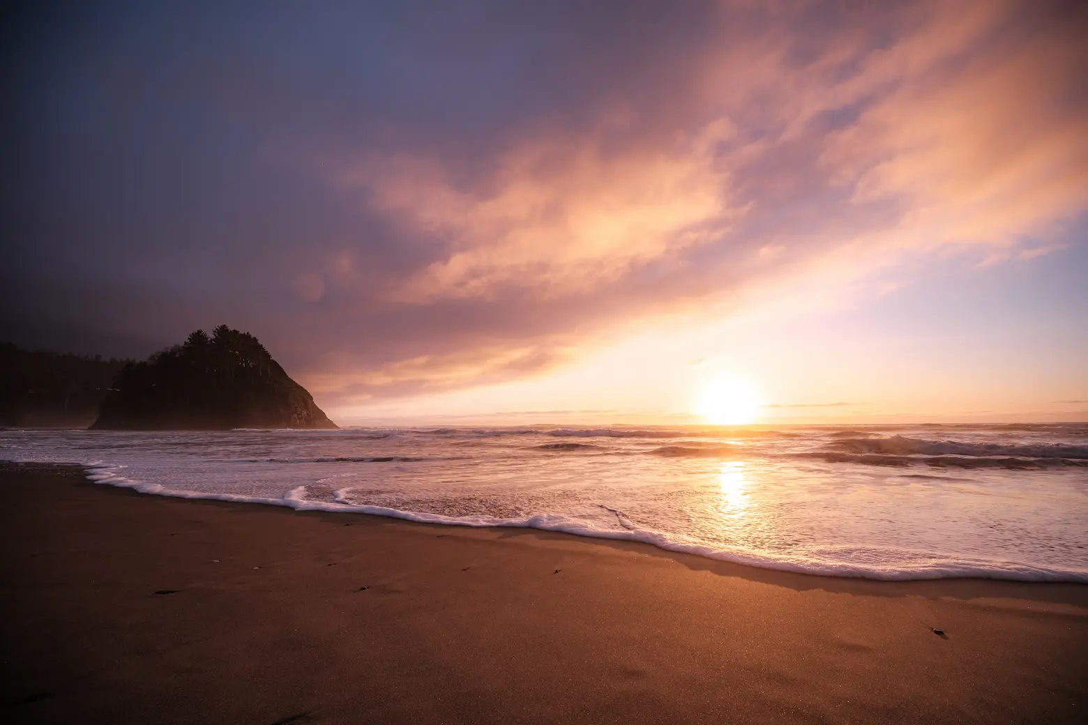 The surf of the ocean approaches the viewer as the sunsets with proposal rock in the background