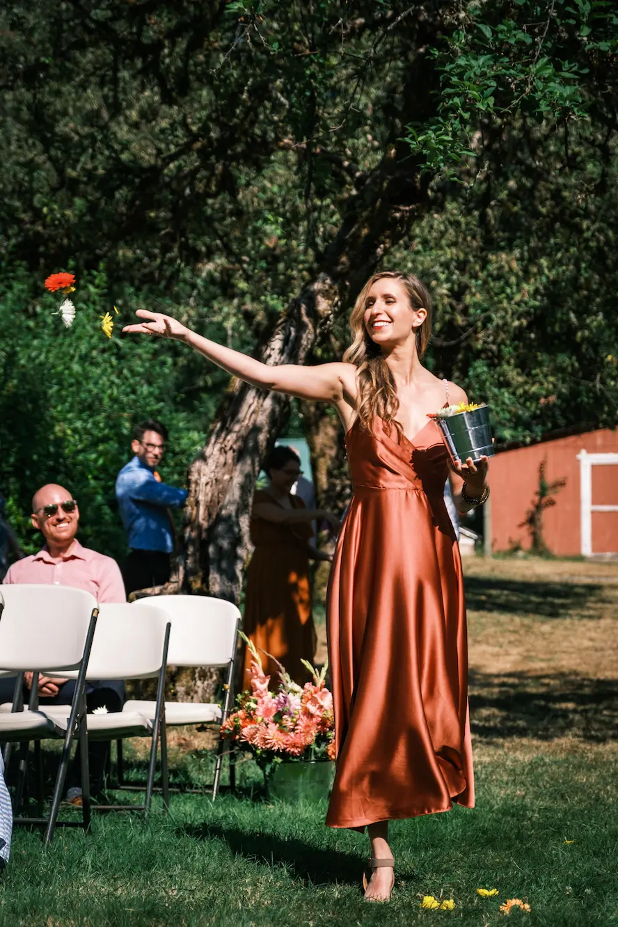 A person in an orange dress tosses flowers at a wedding