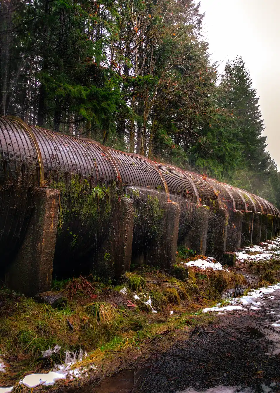 Large wooden pipe leaking water in the woods with snow on the ground