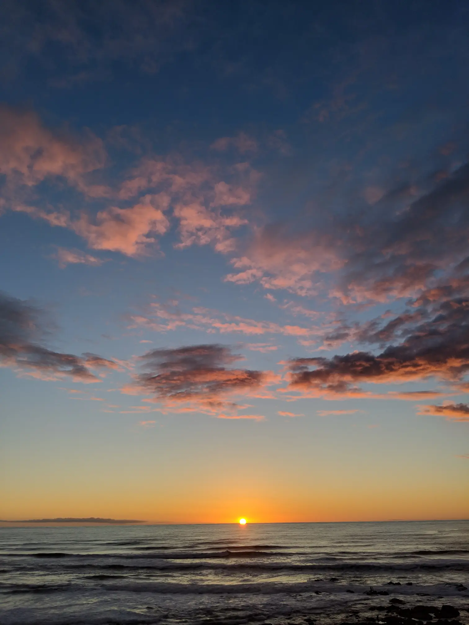 Sunset on the beach with pink clouds and yellow sun over the ocean