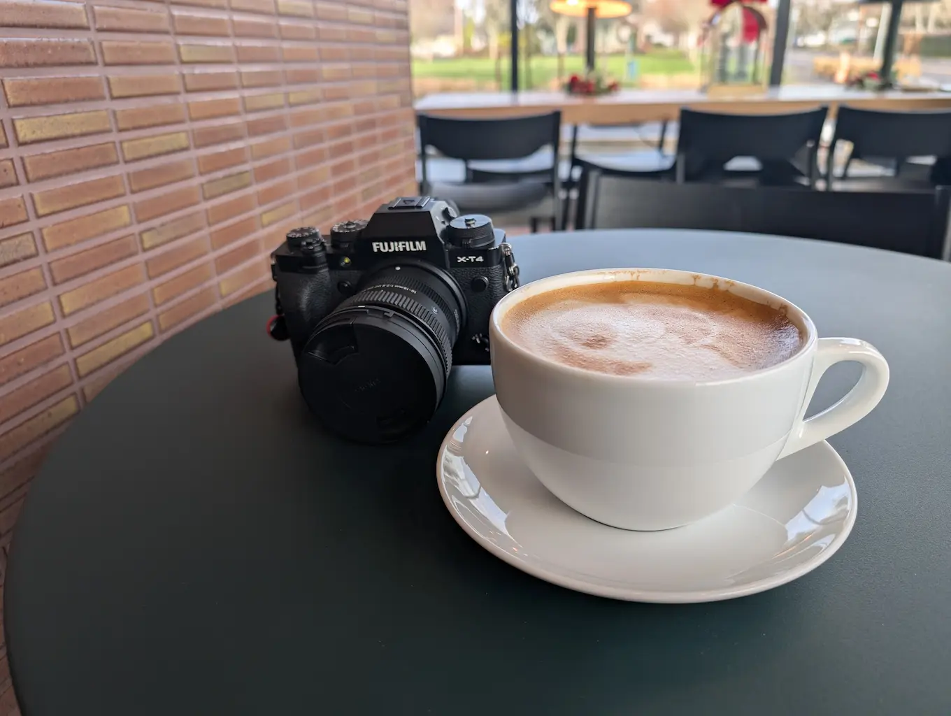 An oat latte on a table at a coffee shop with a digital camera next to it.